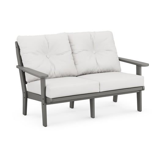 A modern two-seater outdoor loveseat with a gray metal frame and thick, plush white cushions on the seat and back. The POLYWOOD Lakeside Deep Seating Loveseat has wide armrests, uses marine-grade hardware, and.