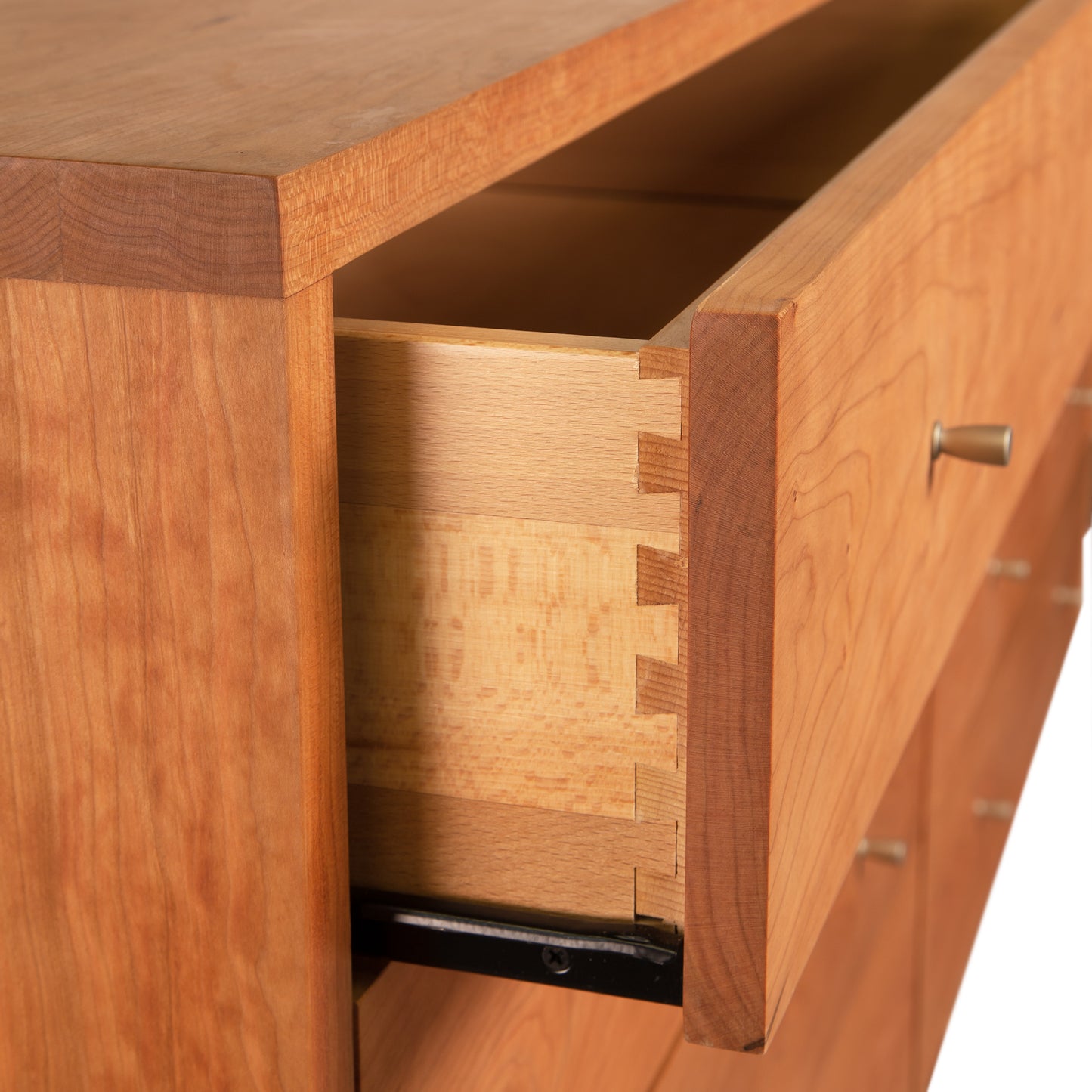 Close-up of an open drawer in a wooden desk, showcasing Vermont Furniture Designs craftsmanship with dovetail joints and a smooth finish, with metal handles visible on other closed drawers.