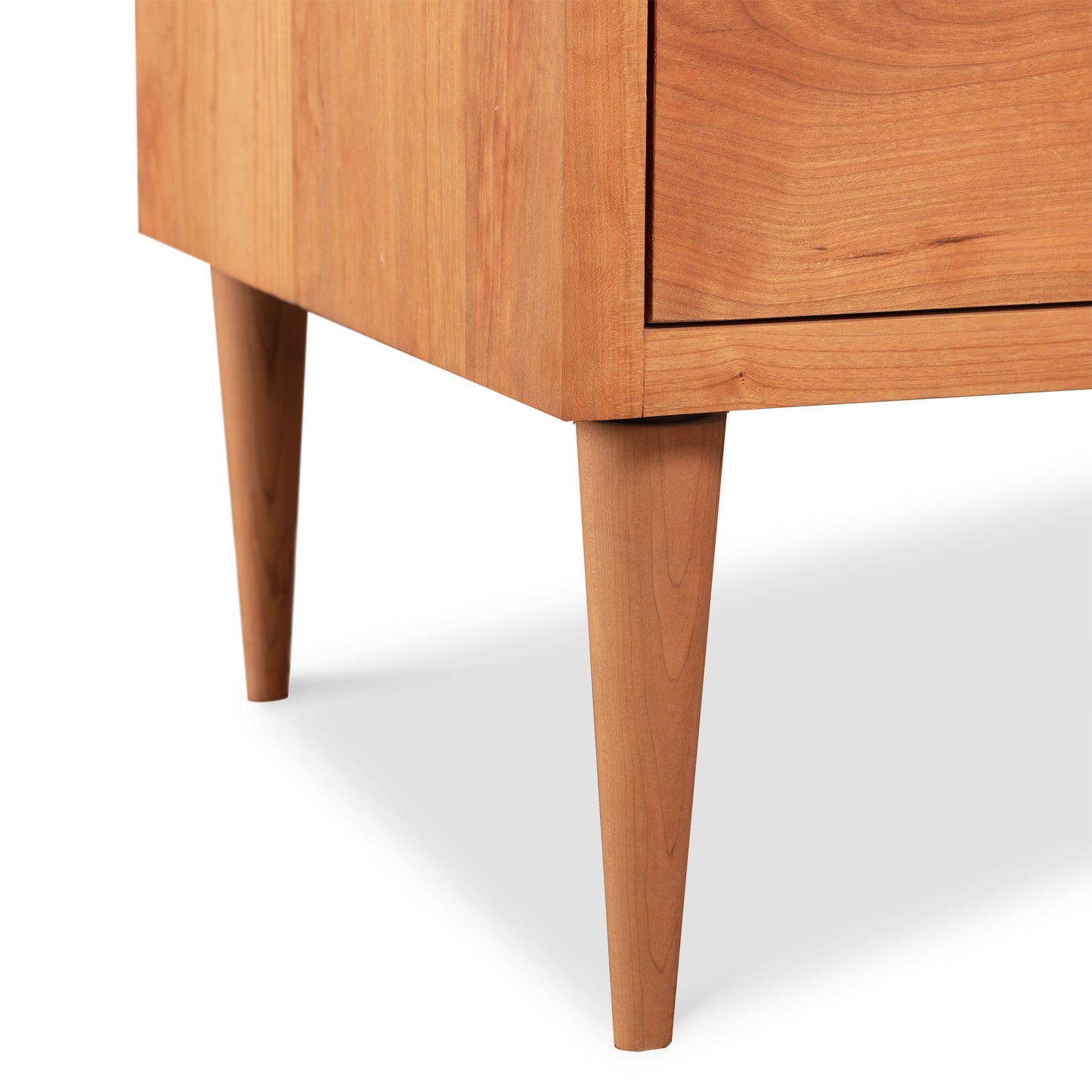 Close-up view of a Larssen 8-Drawer Dresser - Clearance, crafted with natural solid hardwood and showcasing details of its smooth finish and tapered legs, against a white background by Vermont Furniture Designs.