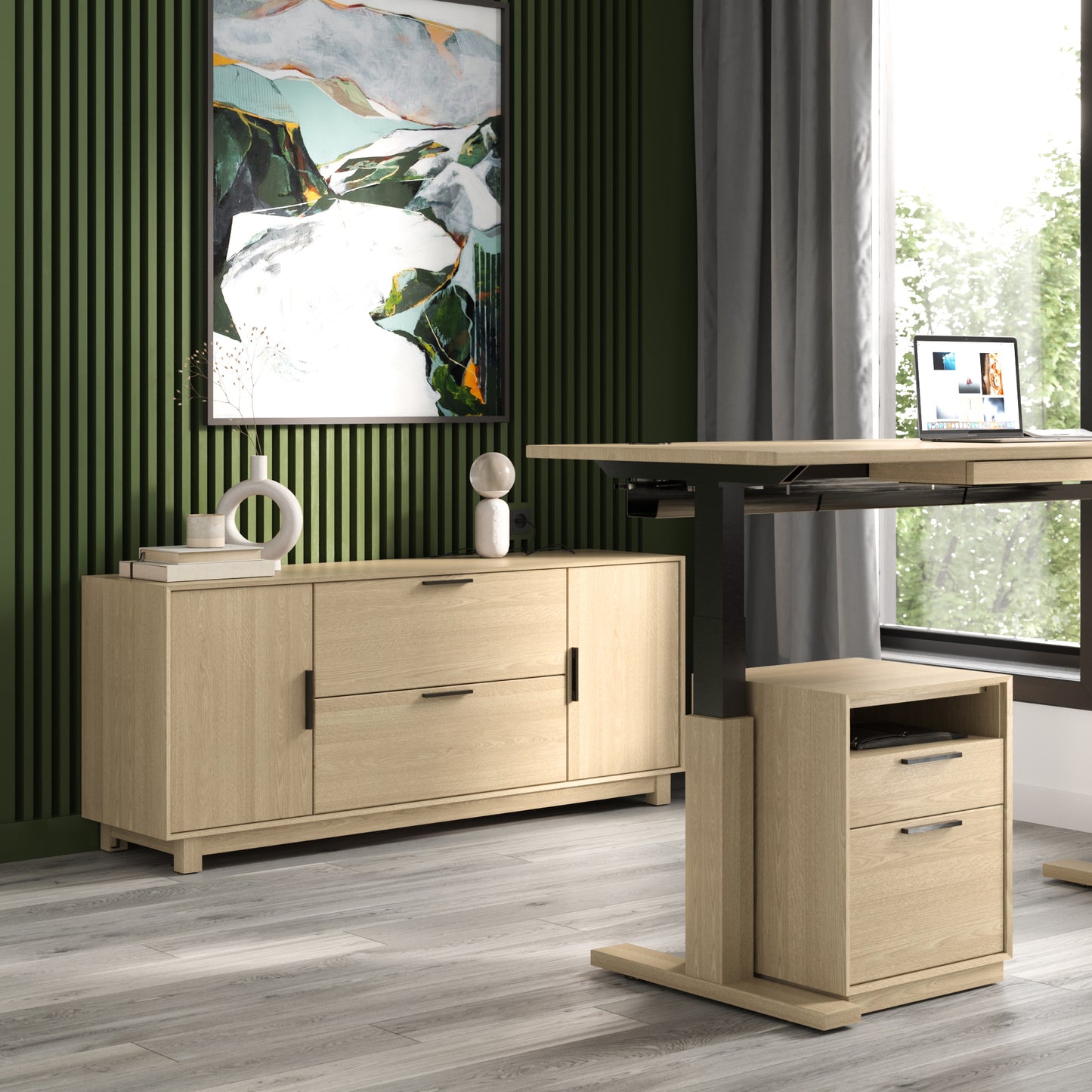 A modern home office featuring green vertical paneling on one wall. Included in the space are a light wooden sideboard, a standing desk with a laptop, and a small matching drawer unit. Natural light pours in through the large window on the right. Above the Linear Office Credenza from Copeland Furniture hangs a colorful abstract painting that adds a mid-century modern touch.