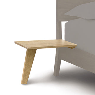 Alt text: Linn Attached Nightstand by Copeland Furniture – Solid Wood Bedside Shelf with Single Leg, Seamlessly Connected to Bed Frame. Made from Sustainably Managed North American Hardwood, Minimalist Design in Light Wood Finish. Partially Visible Bed with White Mattress and Bedding.