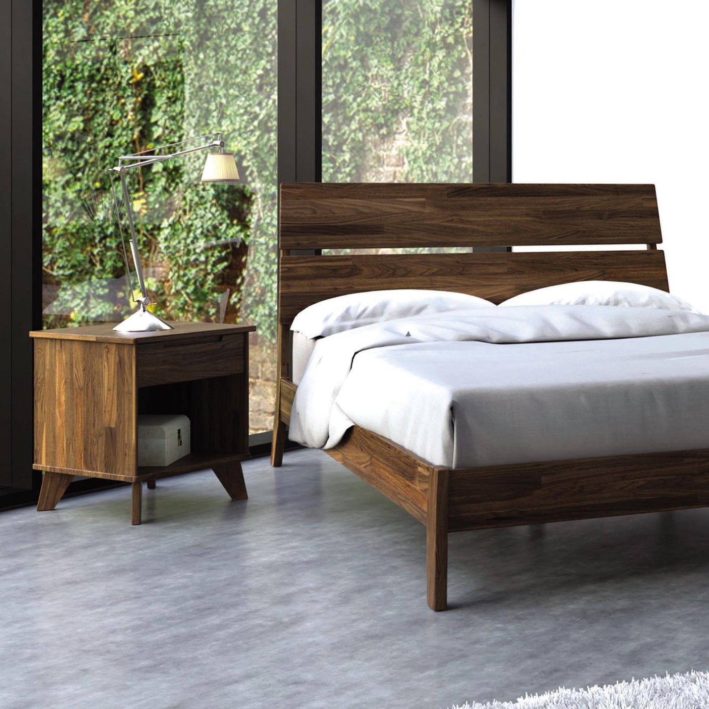 Wooden bed with Copeland's Linn nightstand featuring white bedding and a desk lamp.