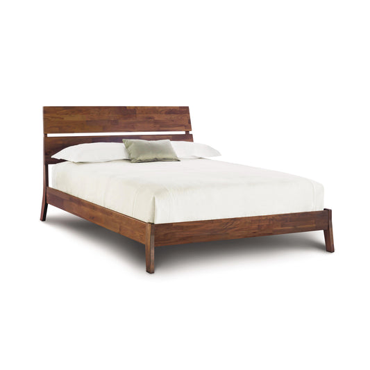 A sustainable Linn Walnut Platform Bed by Copeland Furniture with a slanted headboard, equipped with white bedding and a small pillow, isolated on a white background.