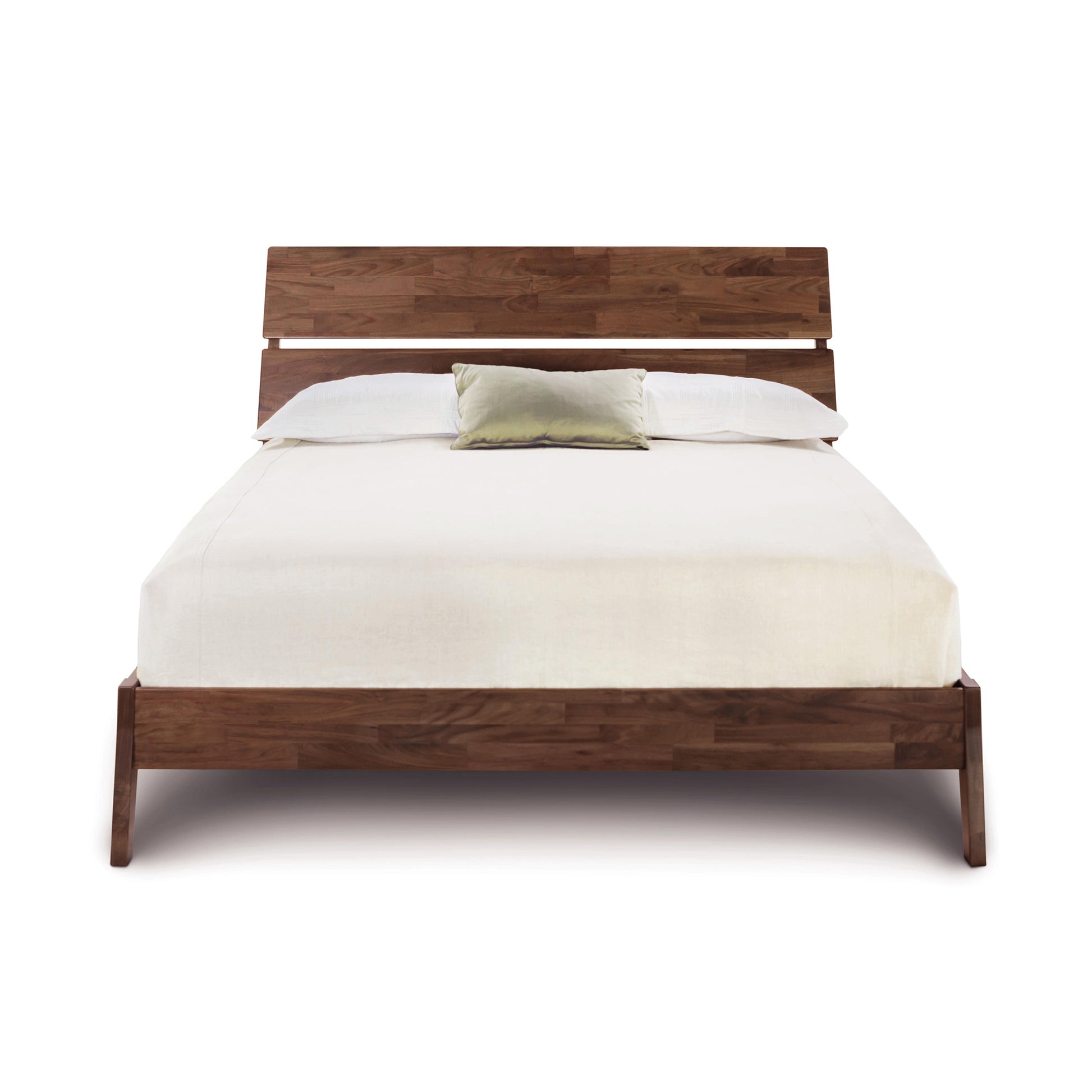 The Linn Walnut Platform Bed by Copeland Furniture, crafted from upcycled wood and featuring a slatted headboard, is centered in the image. The bed is adorned with a white linen sheet and pillows, highlighted by a single light green decorative pillow placed in the middle. This designer piece of furniture stands out against the plain white background.