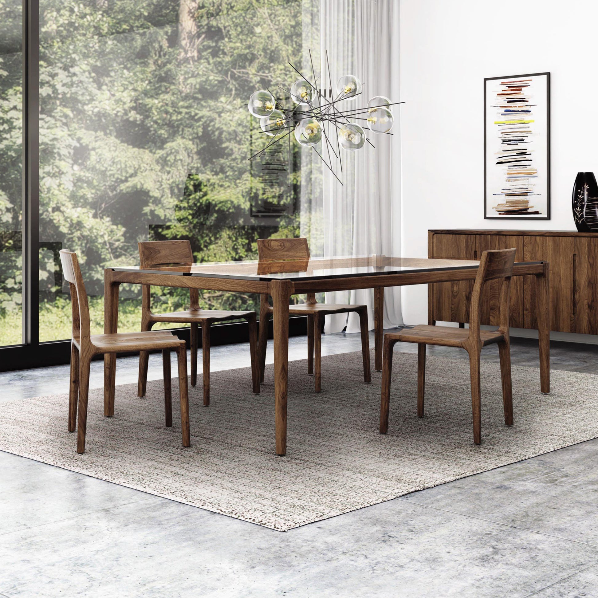 A modern dining room featuring a Copeland Furniture Lisse Glass Top Dining Table with four matching chairs on a light gray rug. A unique chandelier with circular bulbs hangs above. A wooden sideboard fashioned from sustainably-sourced North American black walnut wood sits against the wall, showcasing minimalist design and decor before a large window with a forest view.