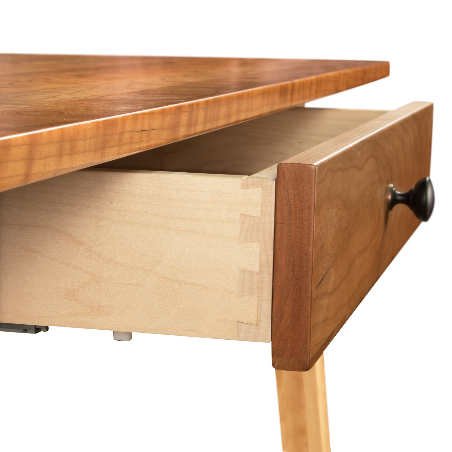 Close-up of a partially open drawer from the Manchester Two-Tone Writing Desk in Cherry and Birch Wood by Vermont Woods Studios, showcasing dovetail joints and a black knob handle. This sustainable, solid wood desk features a glossy cherry surface with light birch legs, ideal for modern home office furniture.