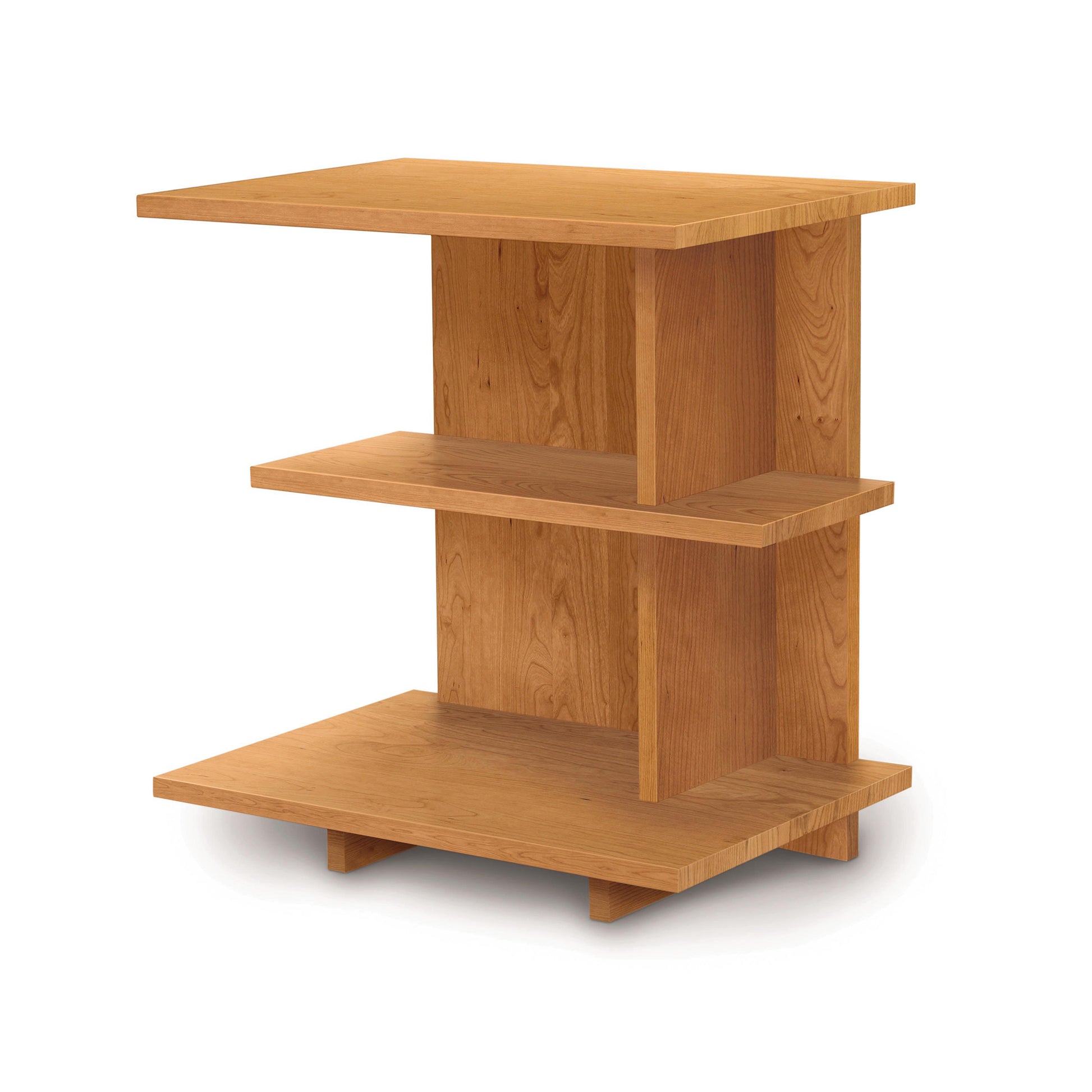 The Mansfield Open Shelf Nightstand by Copeland Furniture features three staggered rectangular shelves with a vertical support structure. The wood boasts a warm, natural finish that blends seamlessly with cherry bedroom furniture, creating a simple and modern appearance.