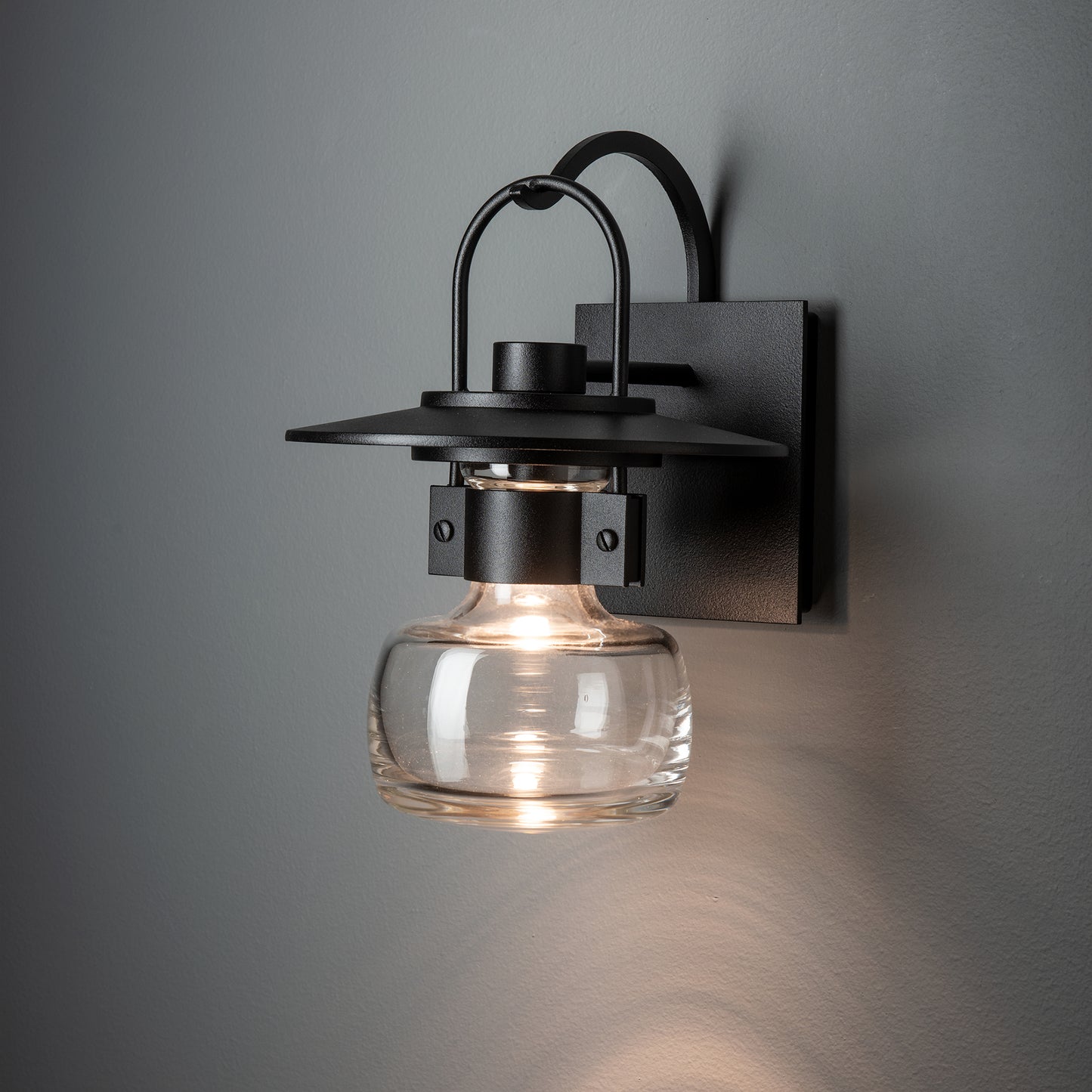 The Mason Outdoor Sconce by Hubbardton Forge features black metal and glass, showcasing artisanal craftsmanship and elegant American-made design.