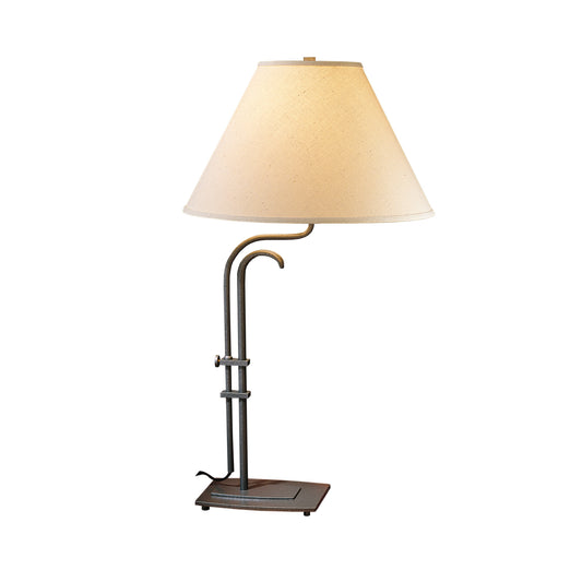A Hubbardton Forge Metamorphic table lamp with a beige shade on it.