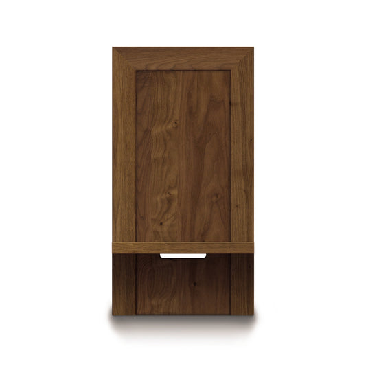 The Moduluxe Attached Nightstand with Shelf from Copeland Furniture's Storage Bed Series features a rectangular door with a small open shelf near the bottom. The wood showcases a natural grain pattern, complemented by a horizontal metallic handle. Its minimalist design with clean lines makes it perfect for integration as an attached nightstand.