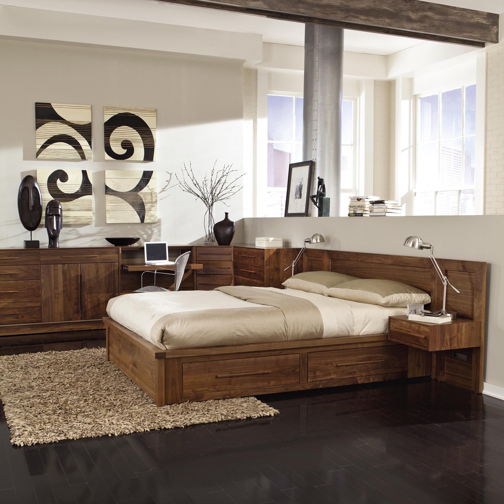 A modern bedroom features a Copeland Furniture Moduluxe Storage Bed with Panel Headboard - 35" Series, handmade in Vermont, with built-in storage drawers and attached nightstands. The room includes dark hardwood flooring, a shag rug, abstract wall art, an eco-friendly desk with a computer, and large windows allowing natural light.