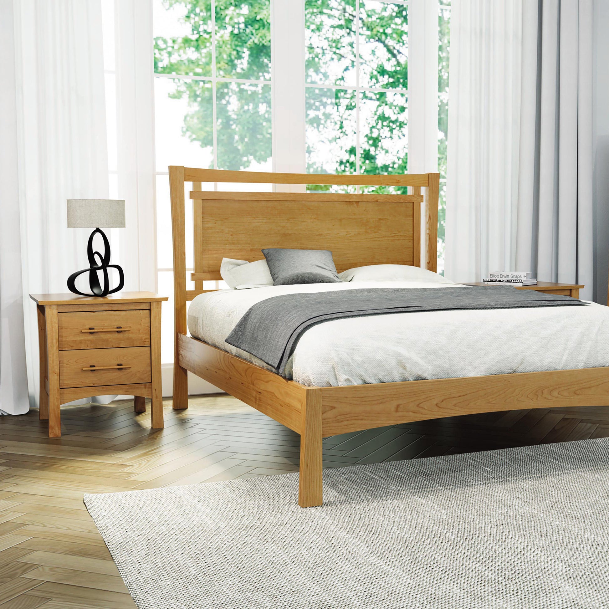 Cherry wood bed with gray and white bedding alongside a Monterey nightstand by Copeland Furniture.