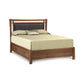 A modern Copeland Furniture Monterey Storage Bed with Upholstered Headboard crafted from solid cherry wood, with an eco-friendly padded headboard, including a neutral-toned bedding set and two decorative pillows.