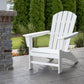 A POLYWOOD Nautical Adirondack Chair, crafted from durable POLYWOOD® lumber, is elegantly positioned on a stone patio adjacent to a brick and stone wall. In the backdrop, well-maintained evergreen trees and a small grassy area create an inviting setting for outdoor relaxation.