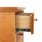 A Lyndon Furniture New England Shaker 3-Drawer Nightstand with Arched Base has a drawer open in its wooden dresser.