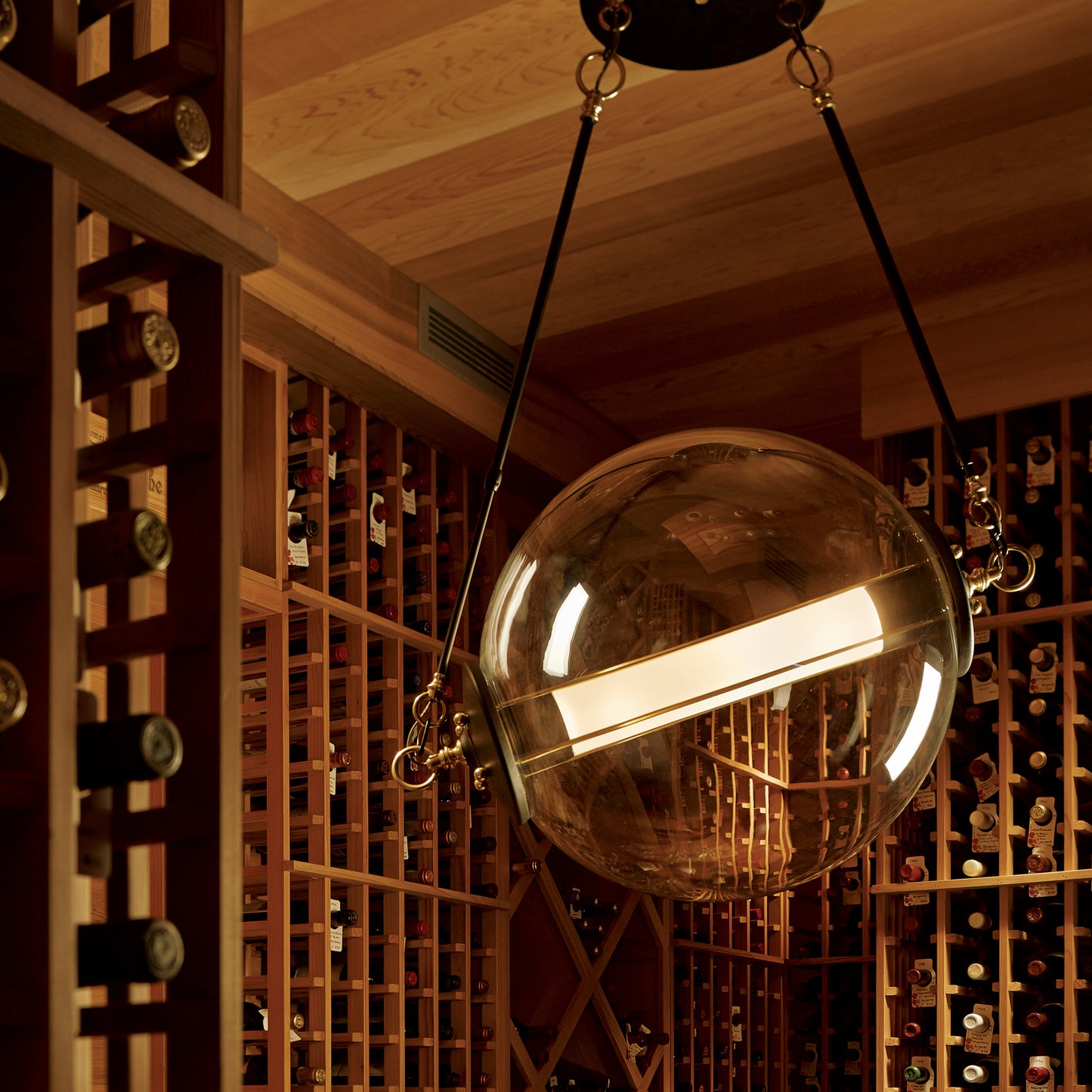A room with Hubbardton Forge pendant lighting and a lot of wine bottles.