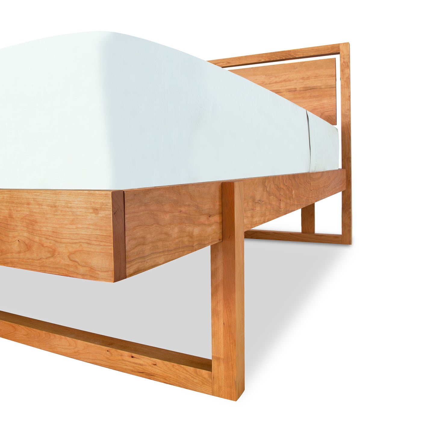 A sustainably harvested cherry wood Pendant Bed frame from Vermont Furniture Designs with a simple design, featuring a mattress with a light blue sheet on it, isolated on a white background.