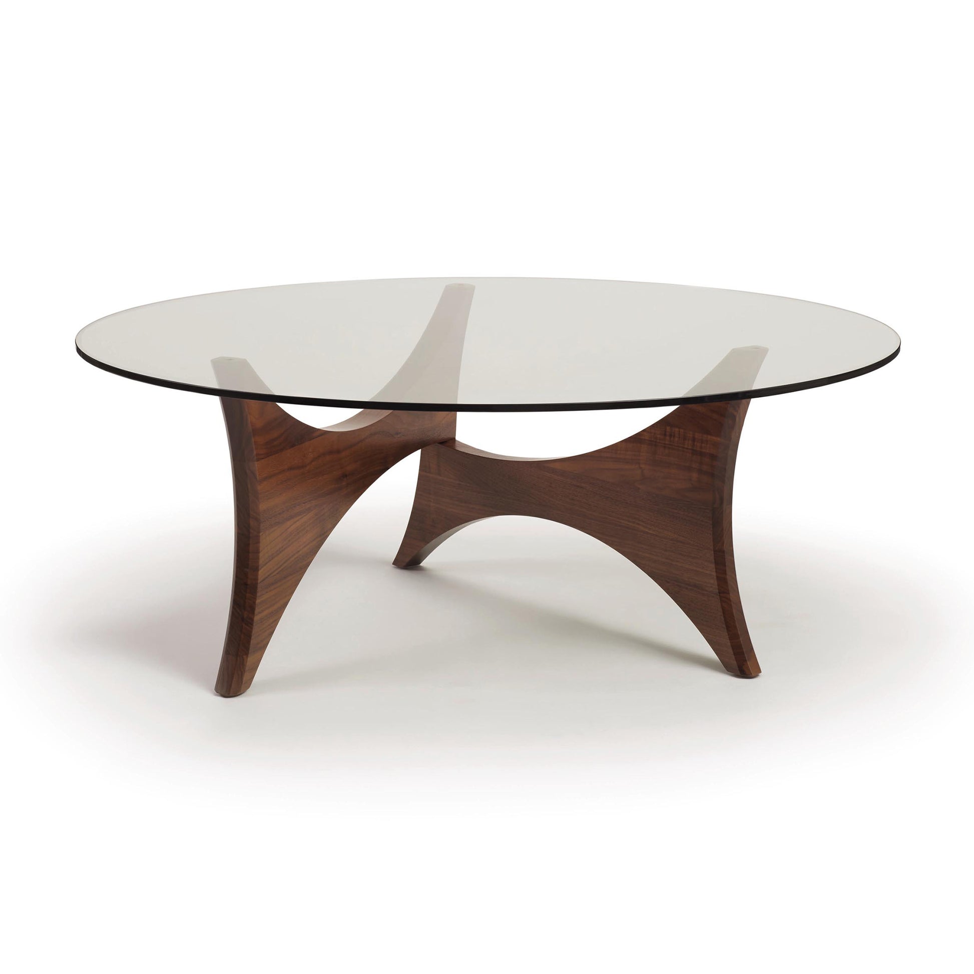 A modern Copeland Furniture Pivot Round Coffee Table with a tempered glass top and a curved walnut base isolated on a white background.