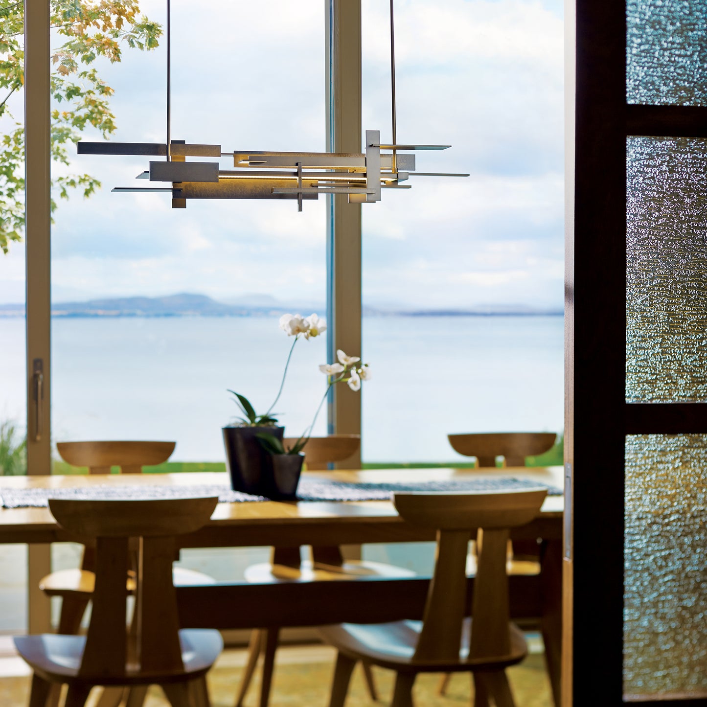 American-made dining table with four chairs, crafted from fine wood, beneath a modern Hubbardton Forge LED pendant. High-quality craftsmanship featured.