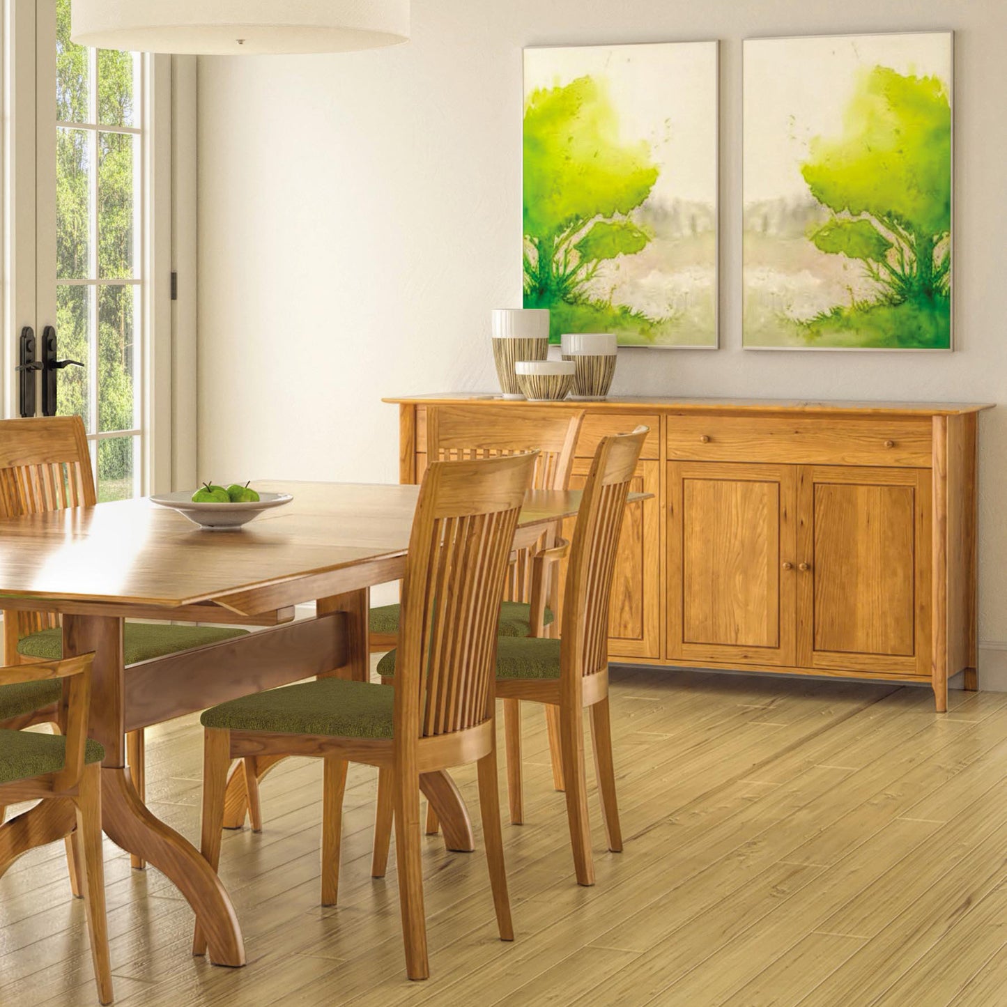 Dining room with a solid wood table and six chairs featuring green cushioned seats. Against the back wall is the Sarah 2-Drawer, 4-Door Buffet from Copeland Furniture, over which hang two abstract paintings with green and yellow tones. Sunlight filters through a glass door on the left.