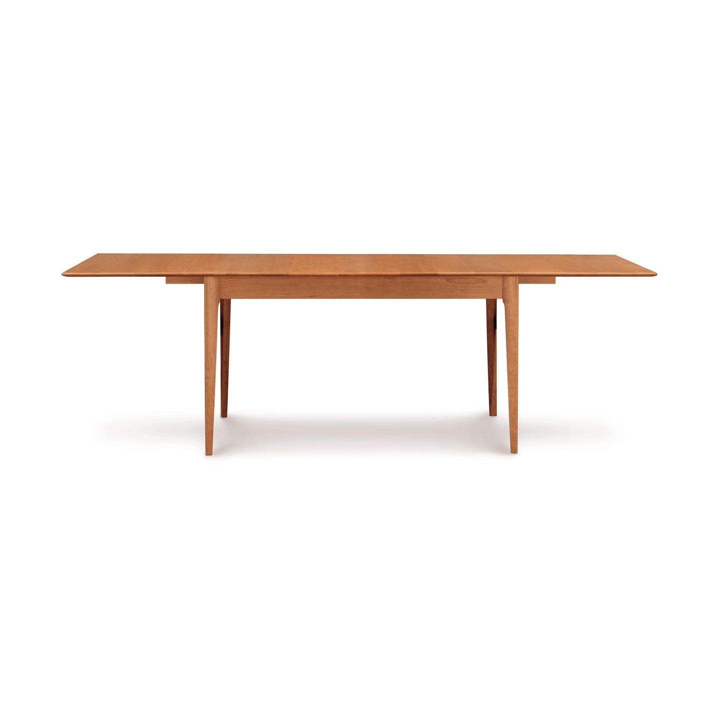 The Sarah Shaker Tapered Leg Extension Table by Copeland Furniture features a minimalist rectangular design crafted from sustainably harvested woods. This table boasts a flat surface and four straight legs, with a light brown finish that enhances its sturdy and functional appearance. Ideal for dining or work, it seamlessly fits into modern bedroom décor against a white background.