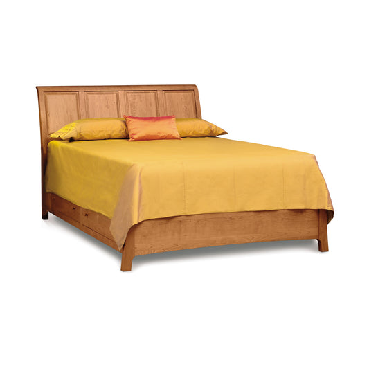 A Sarah Sleigh Storage Bed with a panel headboard, dressed with a plain yellow bedsheet and a single orange pillow against two beige pillows by Copeland Furniture.