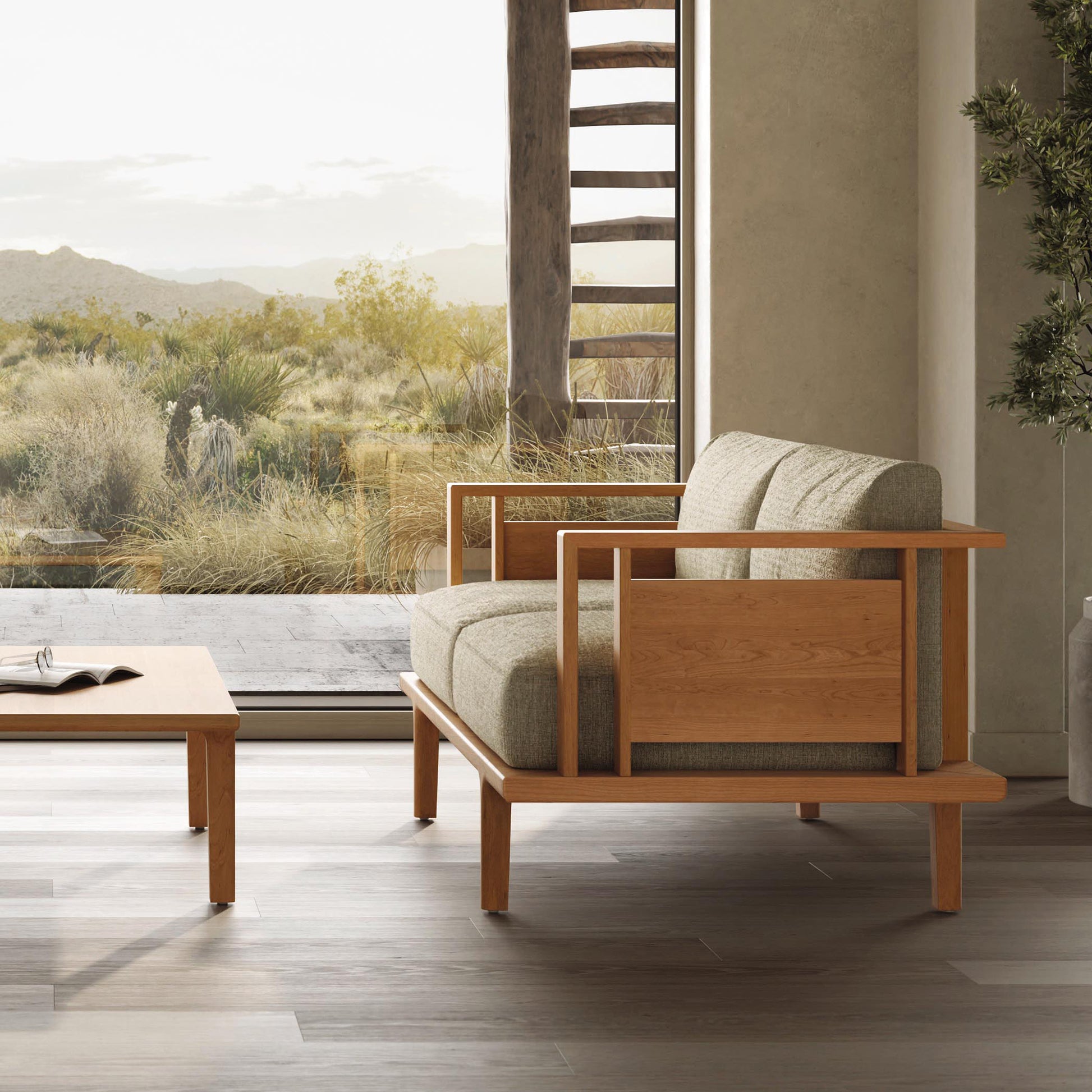 Modern armchair with beige custom upholstery and wooden frame, placed in a room with large windows overlooking a desert landscape.