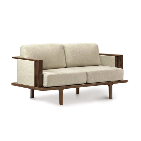A modern Copeland Furniture Sierra Walnut Upholstered Loveseat with Upholstered Panels loveseat with wooden legs and a beige upholstered seat.