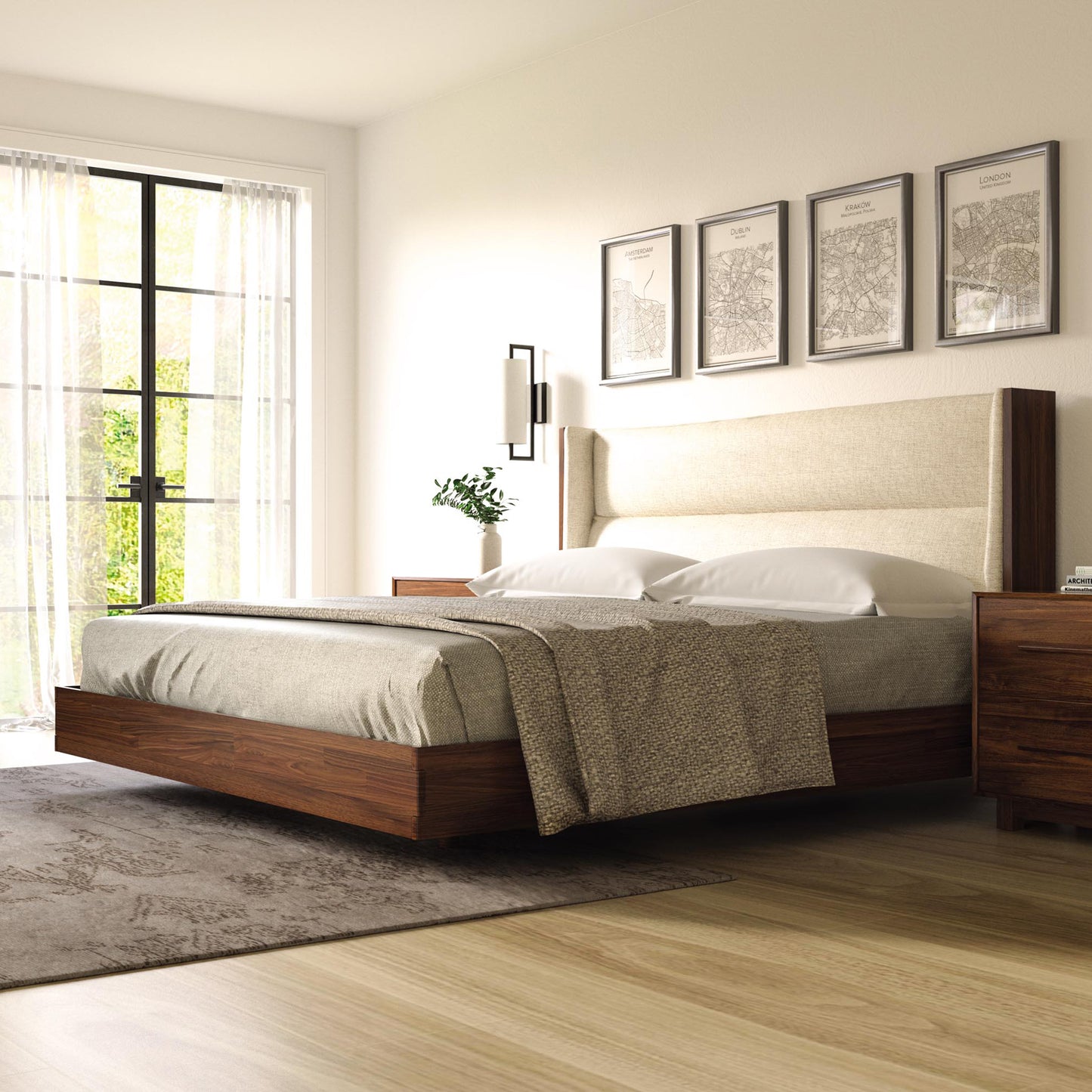 A modern bedroom showcases a large Sloane Floating Bed with a beige upholstered headboard from Copeland Furniture, flanked by matching wooden nightstands. Artwork adorns the wall above the bed, and a large window with curtains adds to the serene atmosphere. A neutral-colored rug lies on the wood floor, completing the look.