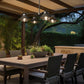 Wooden patio dining table with six chairs featuring a Hubbardton Forge Stowe Outdoor 4-Light Pendant.