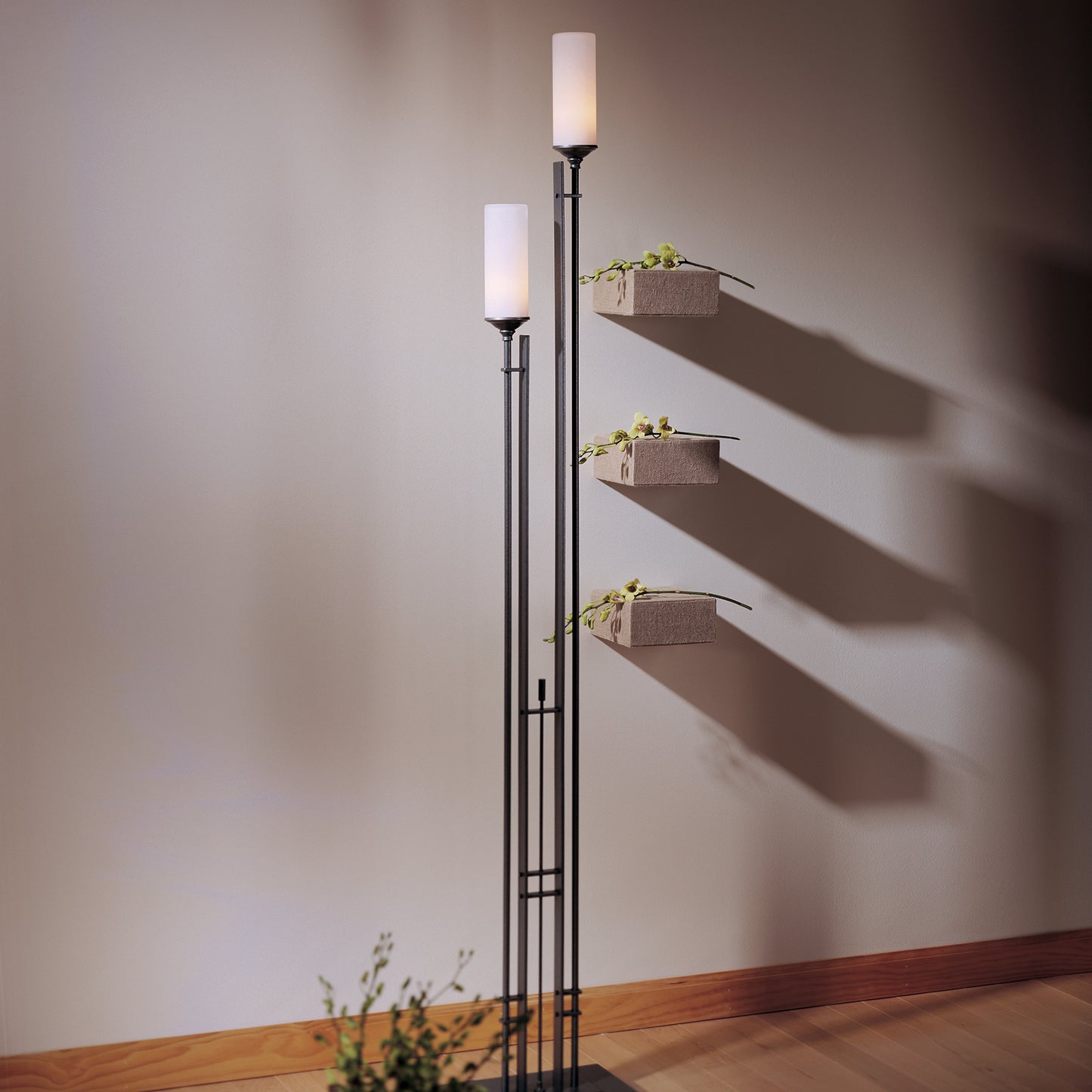 A Hubbardton Forge Tall Metra Twin Floor Lamp with ambient lighting, featuring a decorative plant on top.