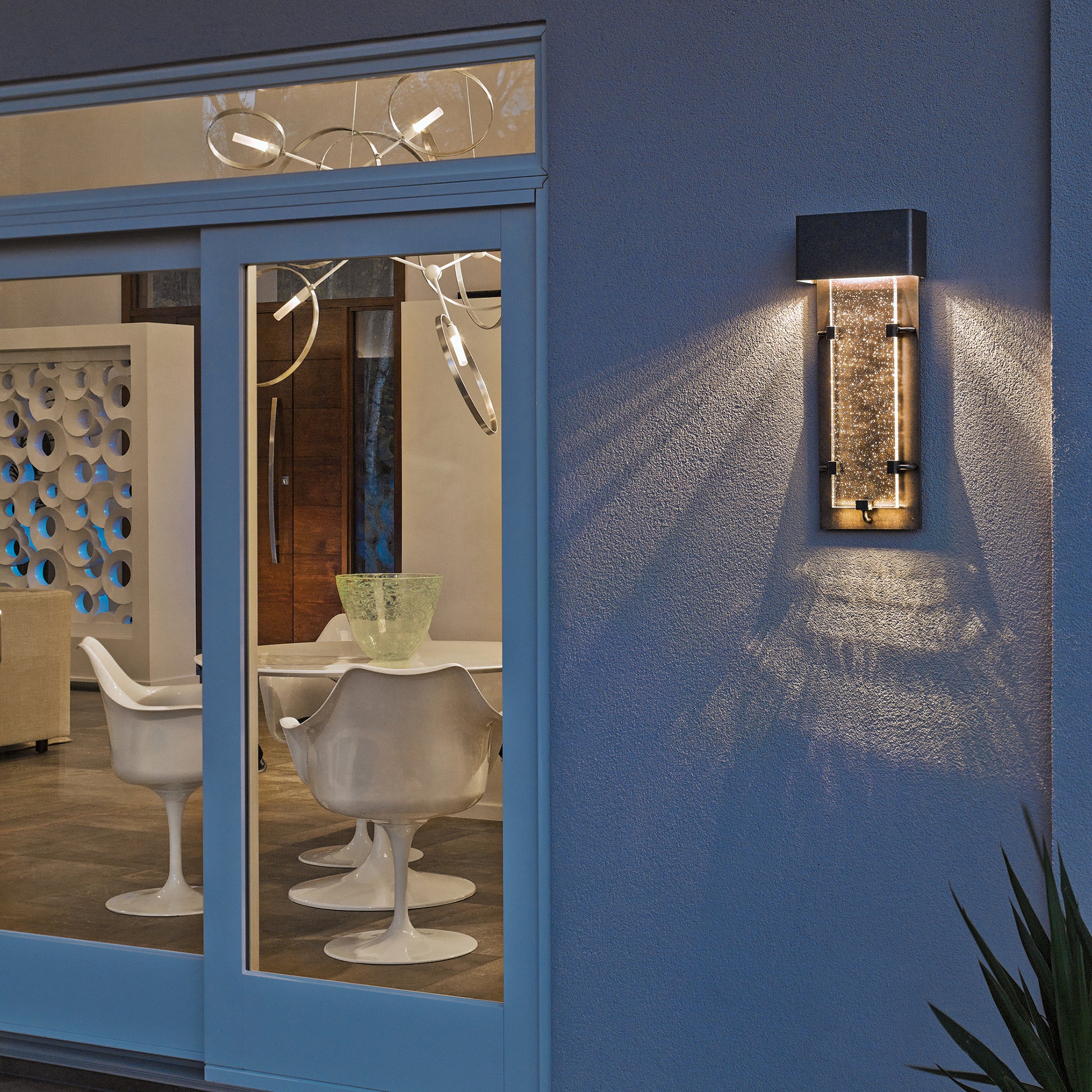 Elegant white chairs are arranged in a modern room, softly illuminated and highlighted by natural light near glass doors.