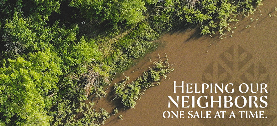 Aerial view of a riverbank partially covered with greenery. The text on the image reads, "Helping our neighbors one sale at a time." The river is muddy, and the greenery is dense and lush along the edge.