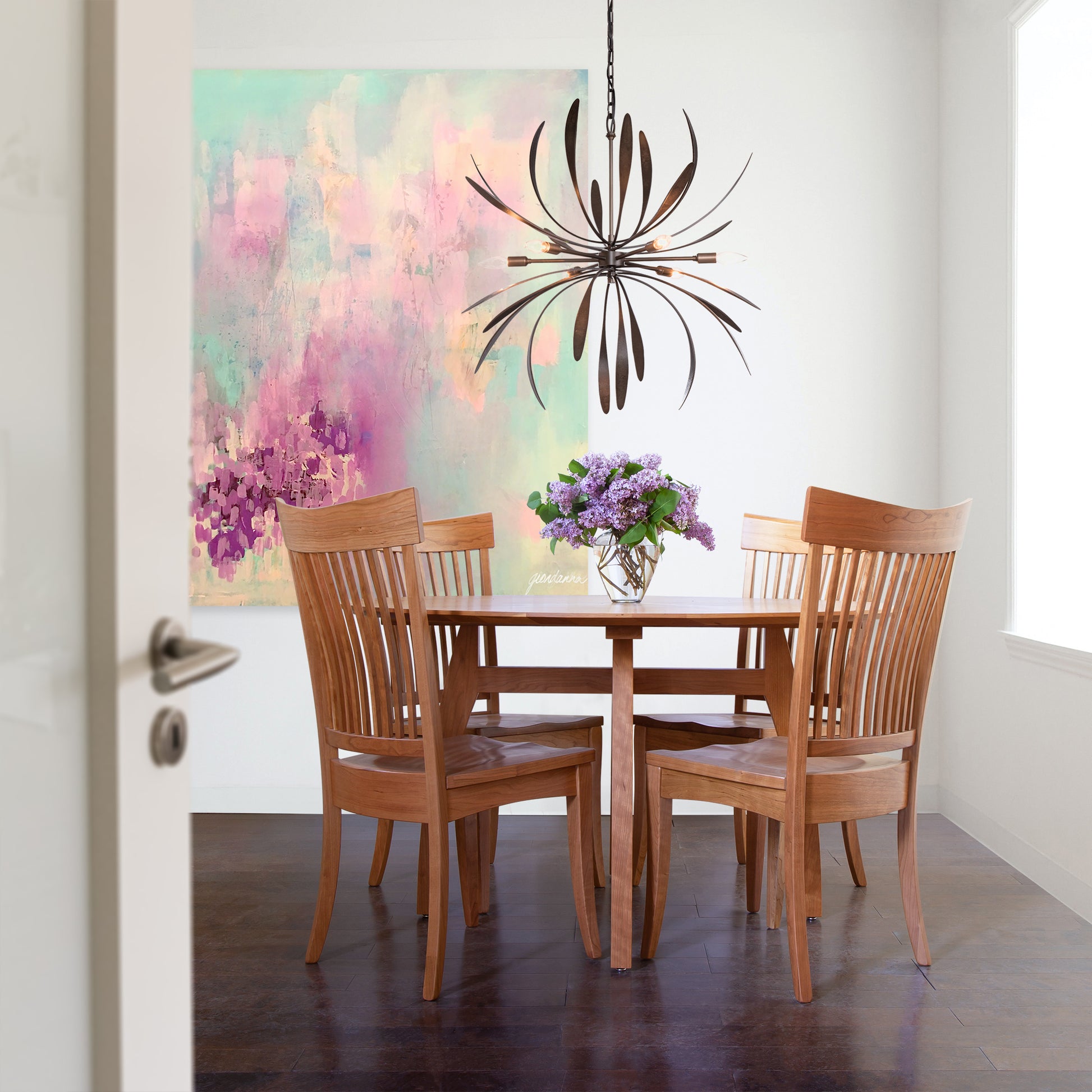 A dining room with a handmade painting on the wall featuring an organic wood Lyndon Furniture Vermont Modern Round Solid Top Pedestal Table.