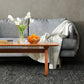 Gray sofa adorned with white blanket; Lyndon Furniture Vermont Modern Trestle Coffee Table featuring vase of tulips and fresh oranges.