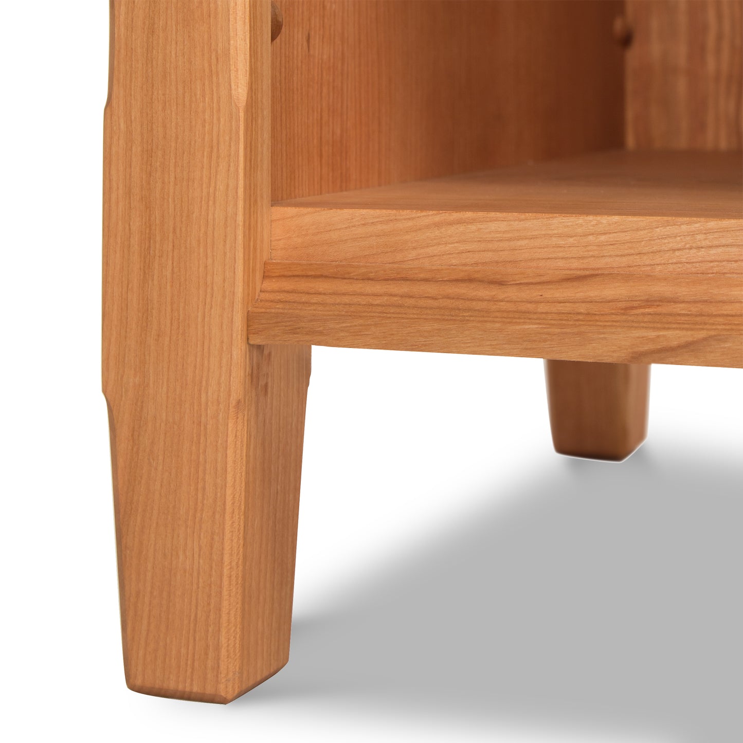 Close-up of a Vermont Shaker 1-Drawer Enclosed Shelf Nightstand by Maple Corner Woodworks, focusing on the detail of the seat and leg junction, with a smooth finish and visible wood grain.