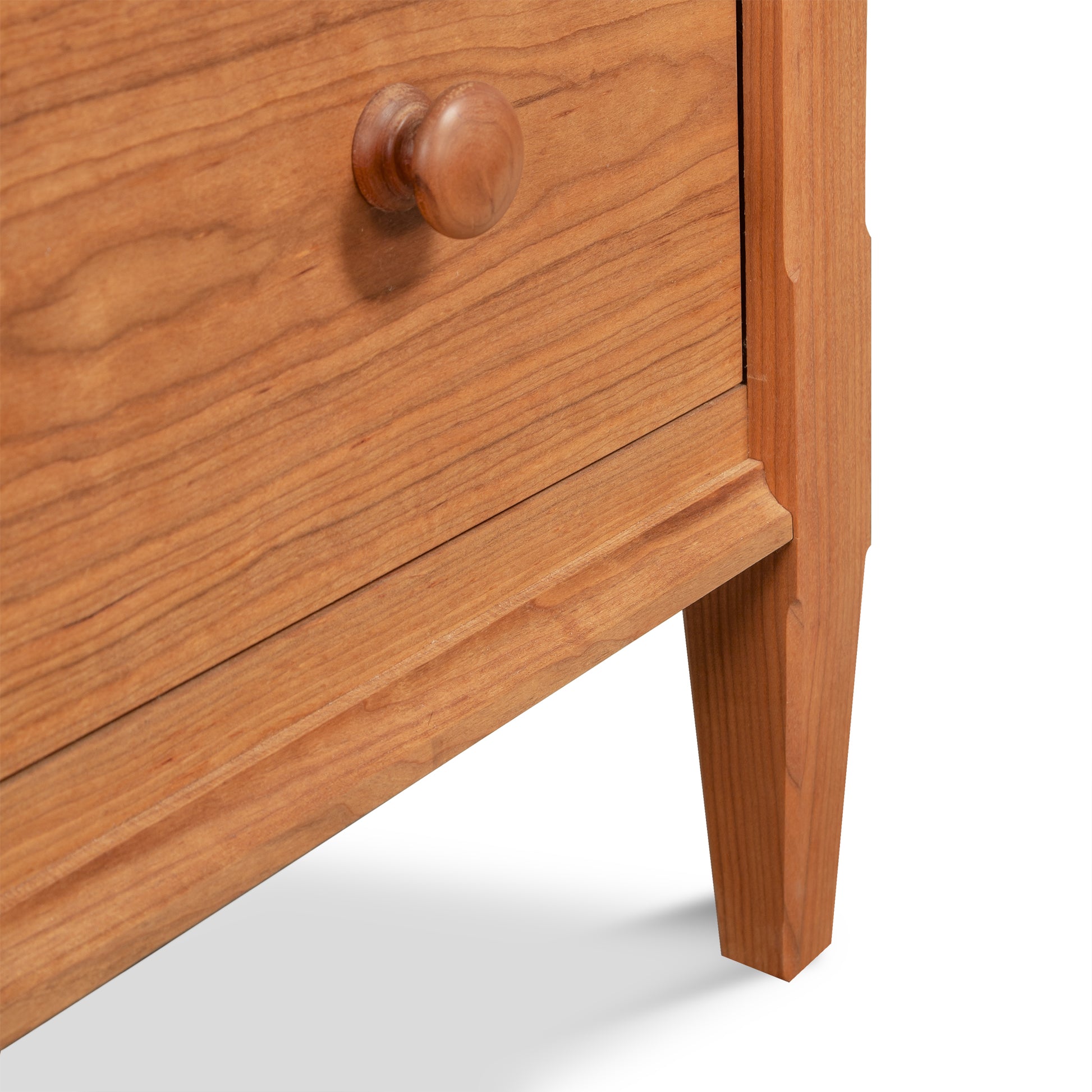 Close-up of the Vermont Shaker 6-Drawer Chest by Maple Corner Woodworks, showcasing a round knob and the smooth grain of handcrafted hardwoods, with a glimpse of its elegant leg—perfect for enhancing bedroom storage.