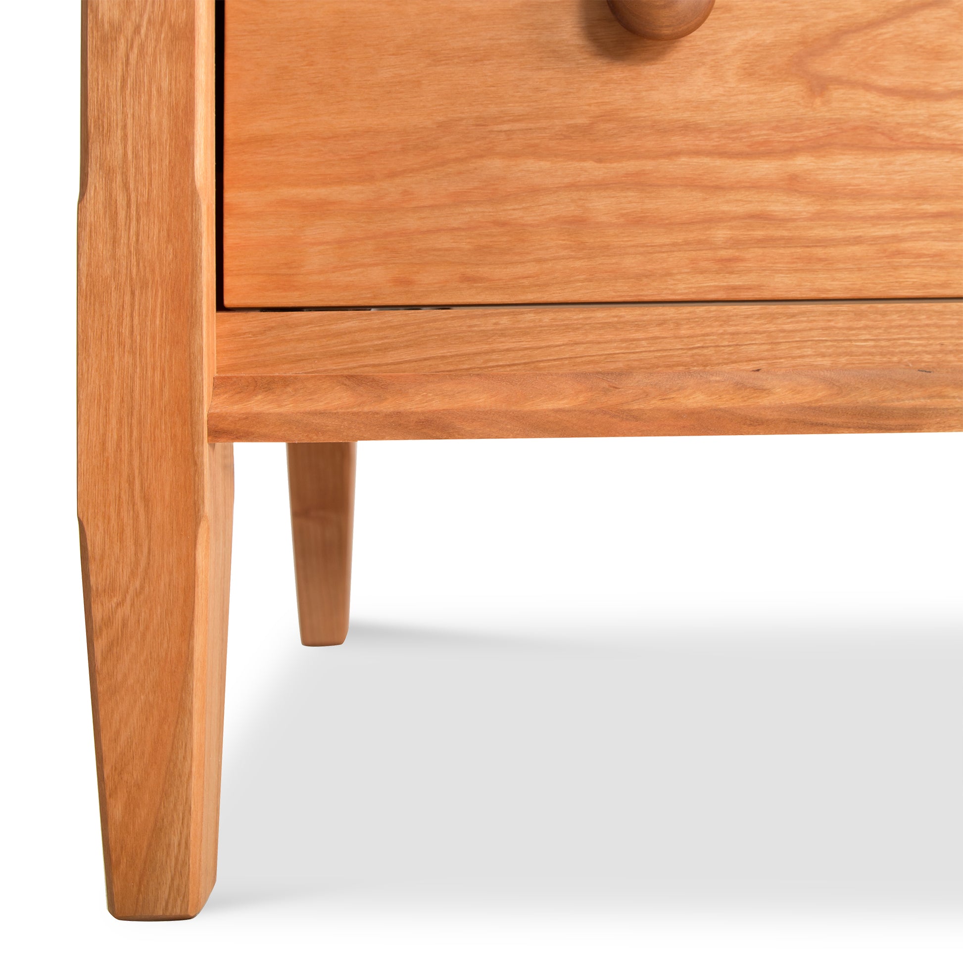 Close-up of a handcrafted wooden Vermont Shaker 7-Drawer Dresser featuring a single drawer with a round knob and angled legs, isolated on a white background by Maple Corner Woodworks.