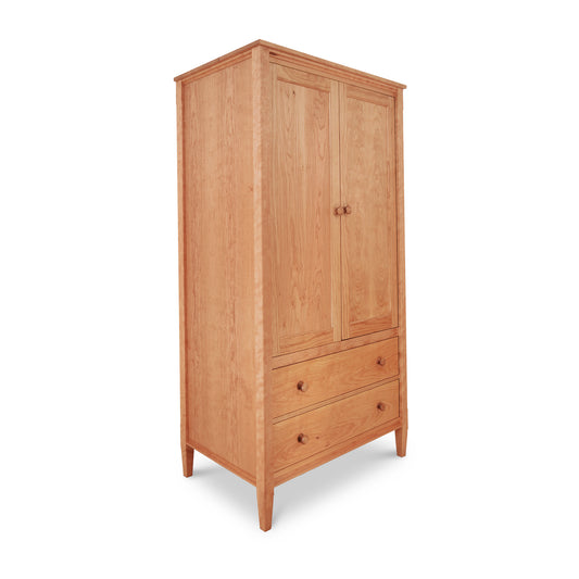 A Vermont Shaker armoire from Maple Corner Woodworks with a natural finish, featuring two doors above a set of two drawers, all with round knobs, and standing on tapered legs.