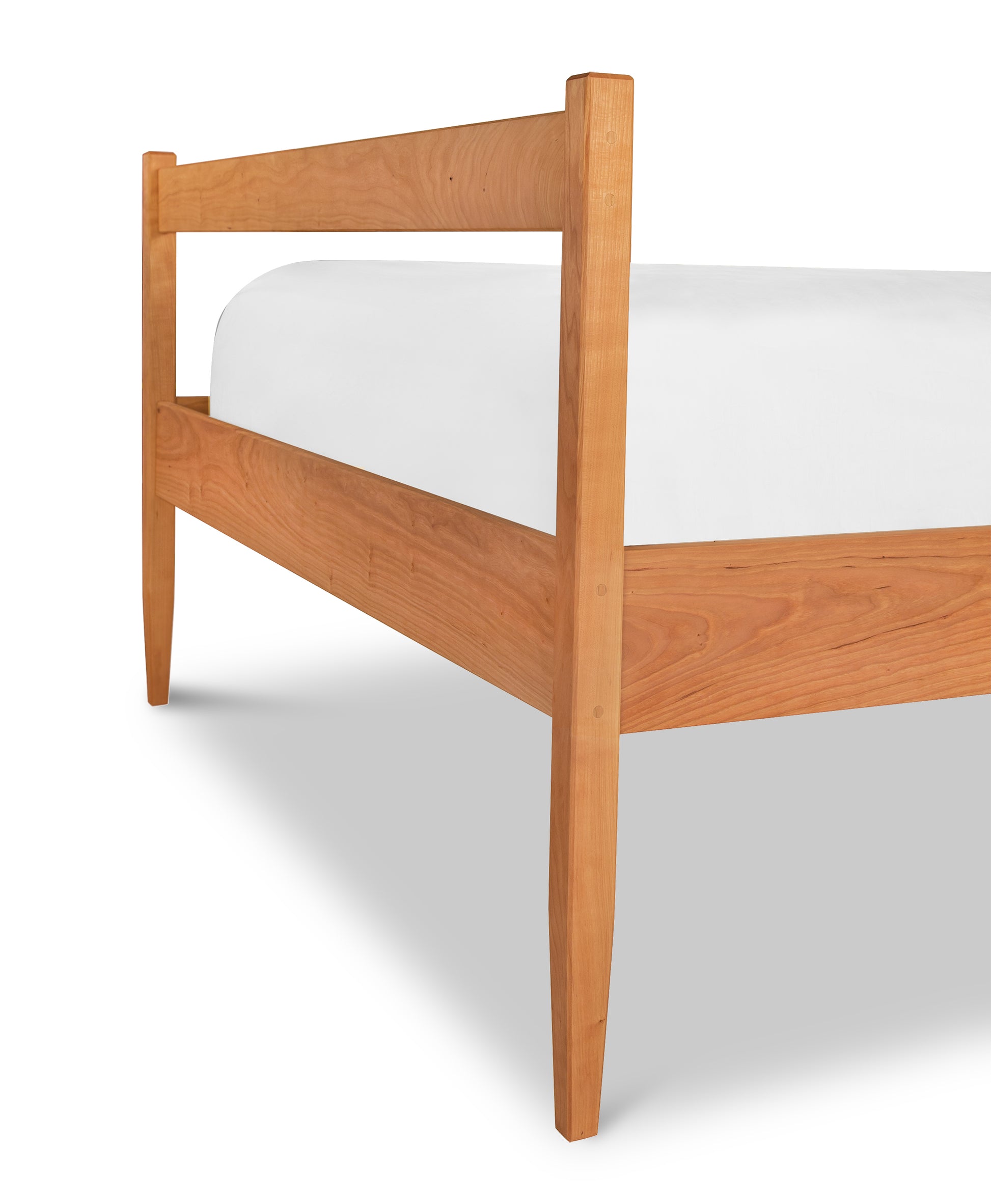 A Vermont Shaker Platform Bed, handmade by Maple Corner Woodworks furniture makers, crafted from solid hardwood and completed with a white sheet on top.