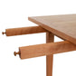 Close-up view of a Maple Corner Woodworks Vermont Shaker Harvest Extension Dining Table showing details of its sliding mechanism and texture of the sustainably harvested woods, isolated on a white background.