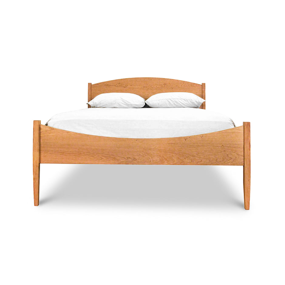 A simple Maple Corner Woodworks Vermont Shaker Moon Bed with a curved headboard and footboard, holding a white mattress and two pillows, isolated on a white background.