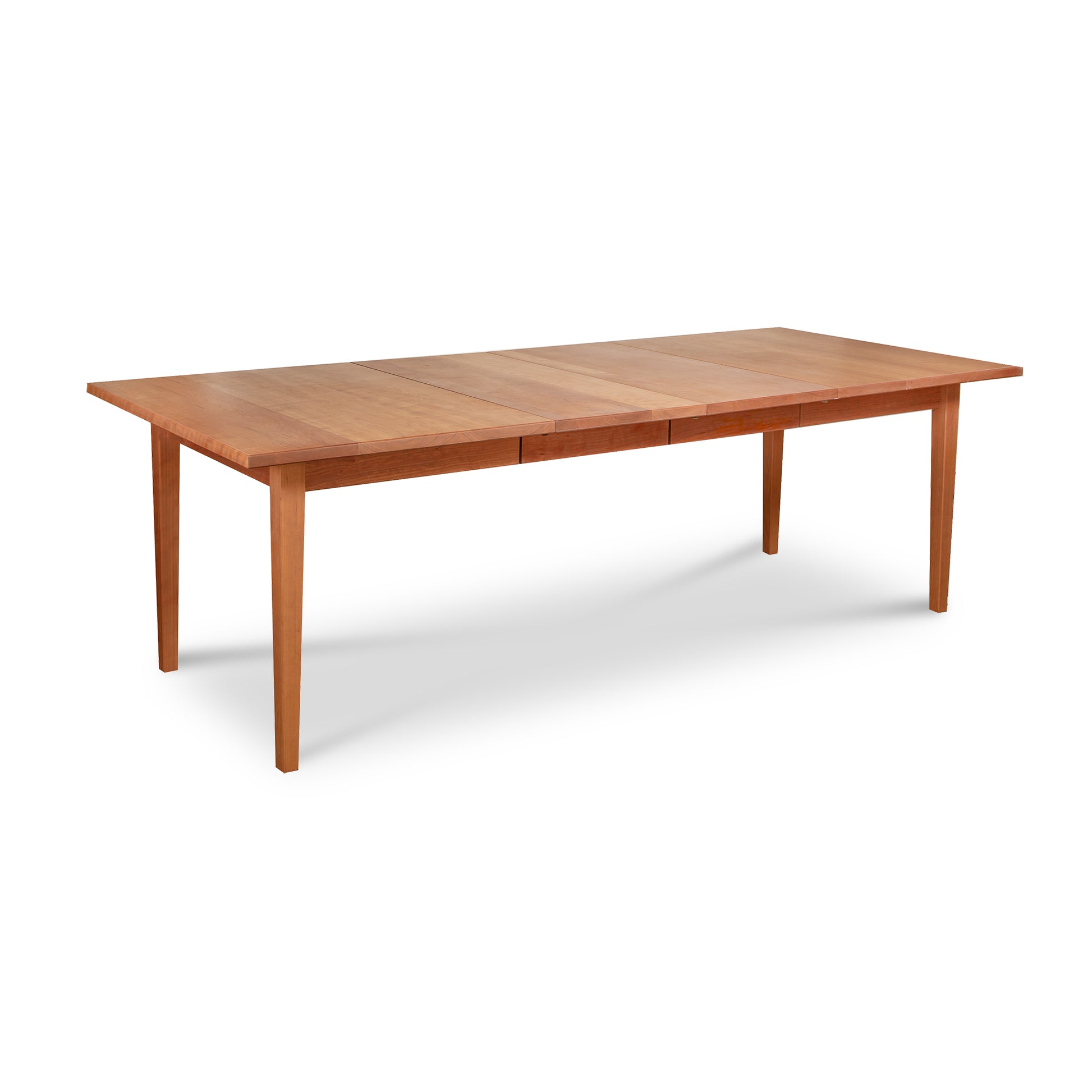 An extended Vermont Shaker Rectangular Extension Dining Table with a natural finish isolated on a white background by Maple Corner Woodworks.