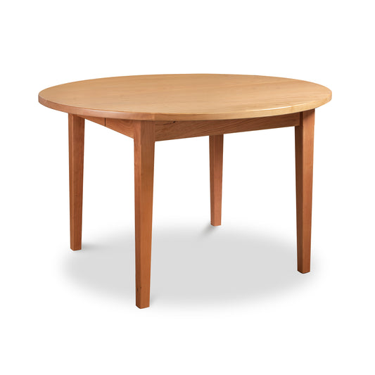 The Vermont Shaker Round Extension Table by Maple Corner Woodworks is a wooden round table featuring four legs, a smooth surface, and natural wood grain. This eco-friendly furniture piece is displayed against a plain white background.