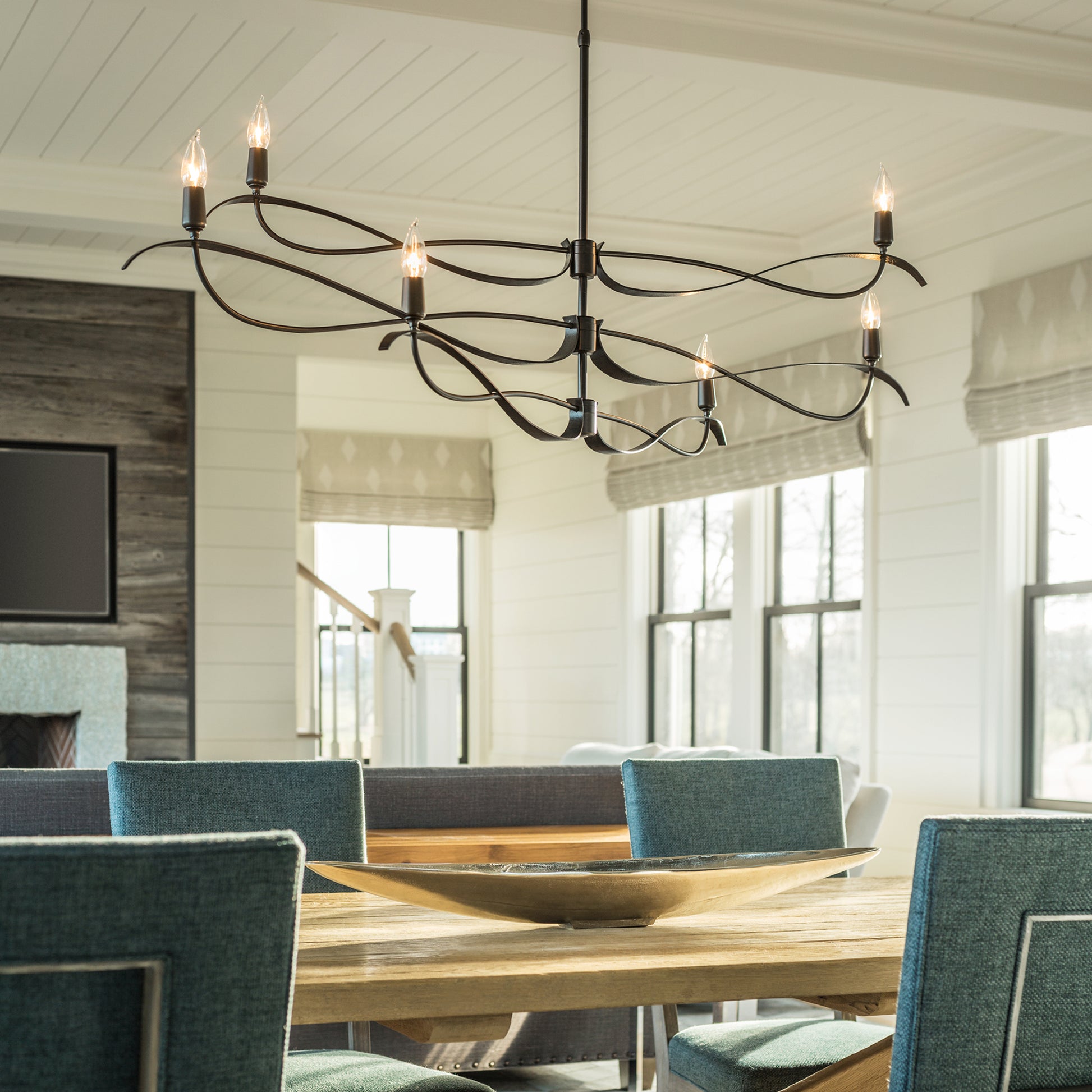 A dining room with modern design, blue chairs, and a Hubbardton Forge Willow 6-Light Small Chandelier.