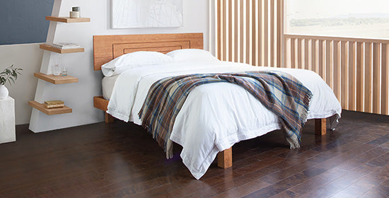 Bedroom interior view, with solid wood bed, wood shelves and plants. 