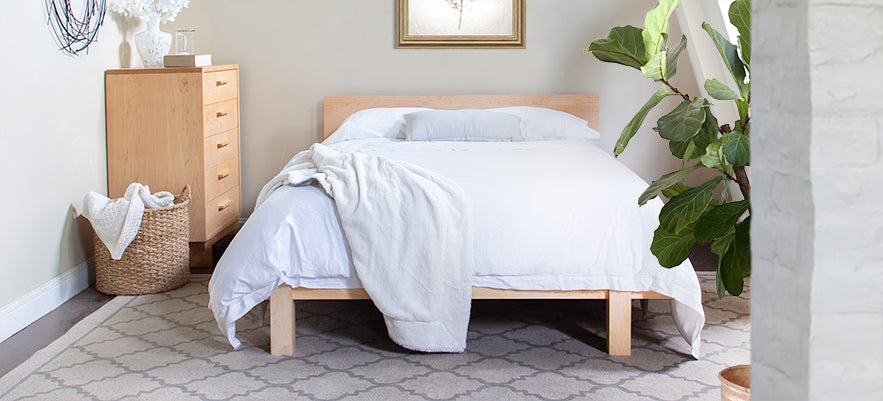 Wooden bed with white bedding and dresser.