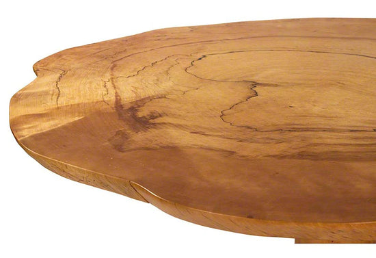 Close-up of a round wooden table with a natural, irregular edge and visible wood grain patterns. The table surface shows a combination of darker and lighter shades of brown with unique lines and textures.