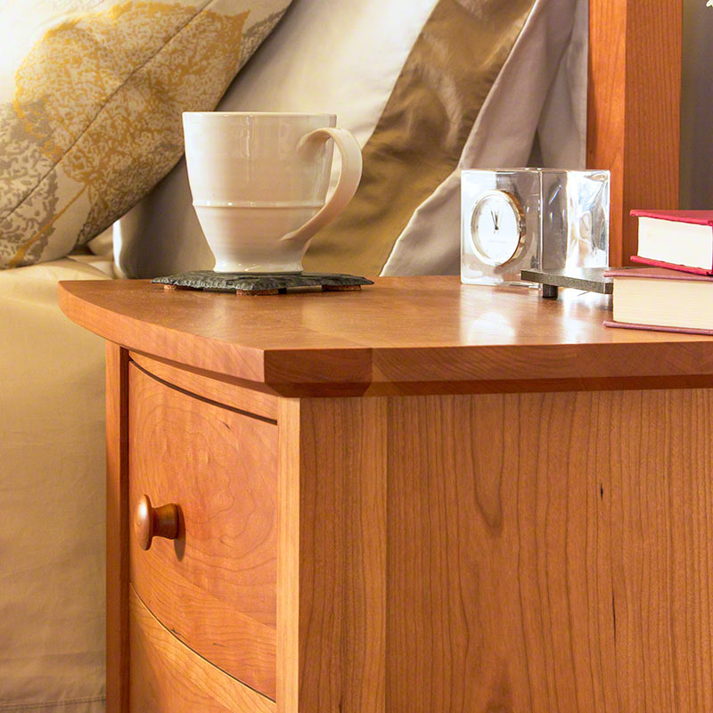 A Lyndon Furniture wooden nightstand with Lyndon Wood Samples books and a Lyndon Wood Samples mug showcasing wood grain patterns.
