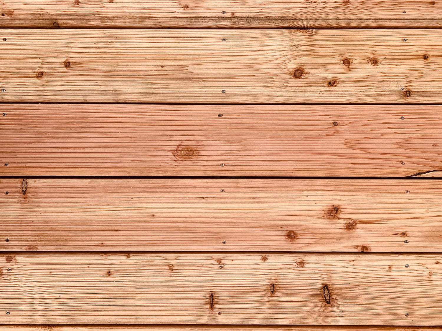 A close-up of a wooden surface composed of multiple horizontal planks. The wood has a light, natural hue with visible grain patterns, knots, and small nail holes. The planks are evenly spaced and appear smooth and well-finished.